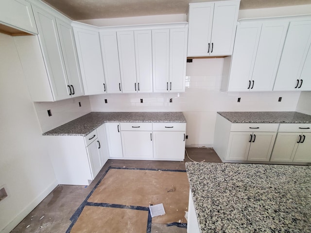 kitchen with stone countertops, decorative backsplash, white cabinetry, and baseboards