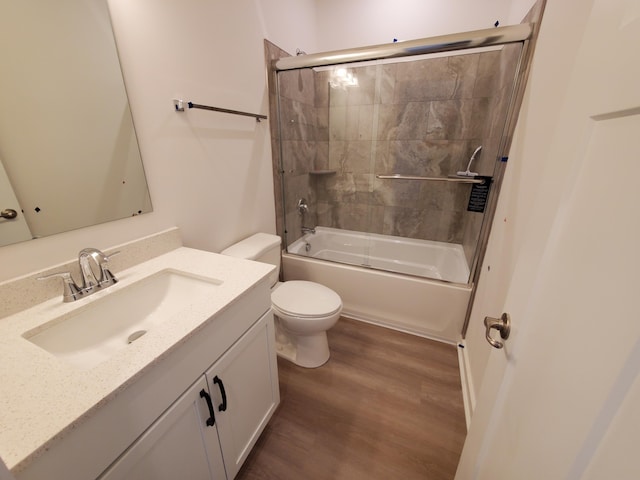 bathroom with wood finished floors, toilet, vanity, and bath / shower combo with glass door