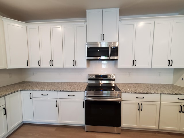 kitchen with appliances with stainless steel finishes, white cabinetry, and light stone counters