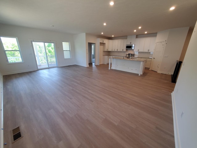kitchen with stainless steel microwave, baseboards, recessed lighting, white cabinets, and wood finished floors