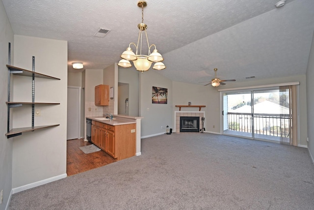 kitchen featuring pendant lighting, ceiling fan with notable chandelier, black dishwasher, tasteful backsplash, and a tiled fireplace