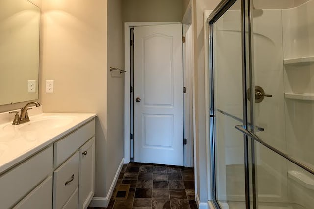 bathroom featuring baseboards, stone finish flooring, a stall shower, and vanity
