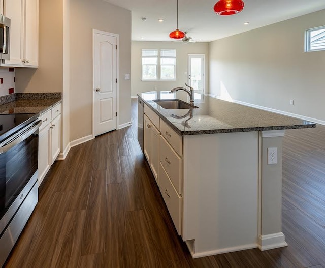 kitchen with dark wood-type flooring, white cabinets, a sink, dark stone countertops, and stainless steel appliances