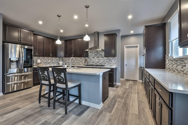 kitchen with stainless steel fridge, dark brown cabinets, wall chimney range hood, pendant lighting, and sink