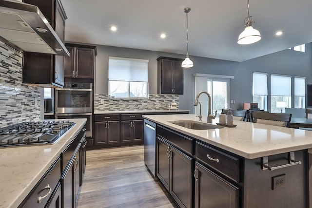 kitchen with pendant lighting, wall chimney range hood, a kitchen island with sink, and stainless steel appliances