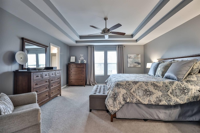 bedroom featuring ceiling fan, a tray ceiling, and light carpet