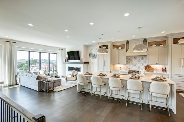 kitchen with a kitchen breakfast bar, dark hardwood / wood-style flooring, decorative light fixtures, a kitchen island with sink, and custom exhaust hood