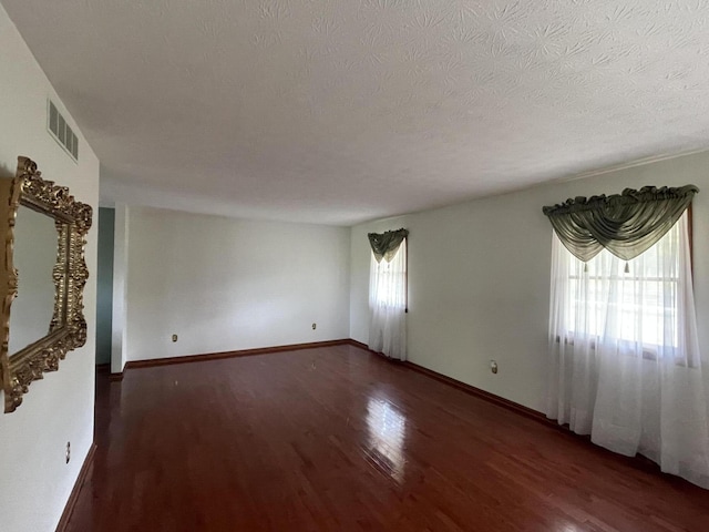 spare room with a textured ceiling, dark hardwood / wood-style flooring, and a wealth of natural light