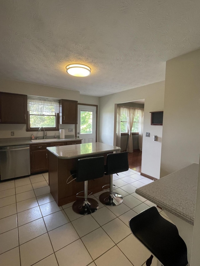 kitchen featuring stainless steel dishwasher, dark brown cabinets, sink, a center island, and a breakfast bar area