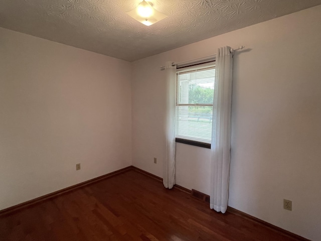 empty room with dark hardwood / wood-style flooring and a textured ceiling