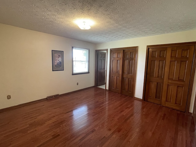 unfurnished bedroom with dark hardwood / wood-style flooring, a textured ceiling, and multiple closets