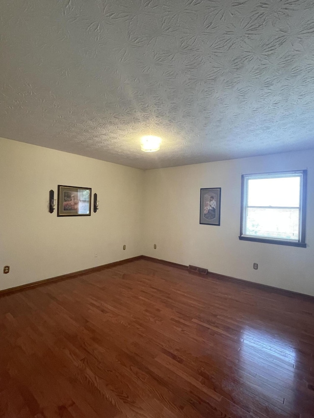 unfurnished room featuring dark wood-type flooring and a textured ceiling