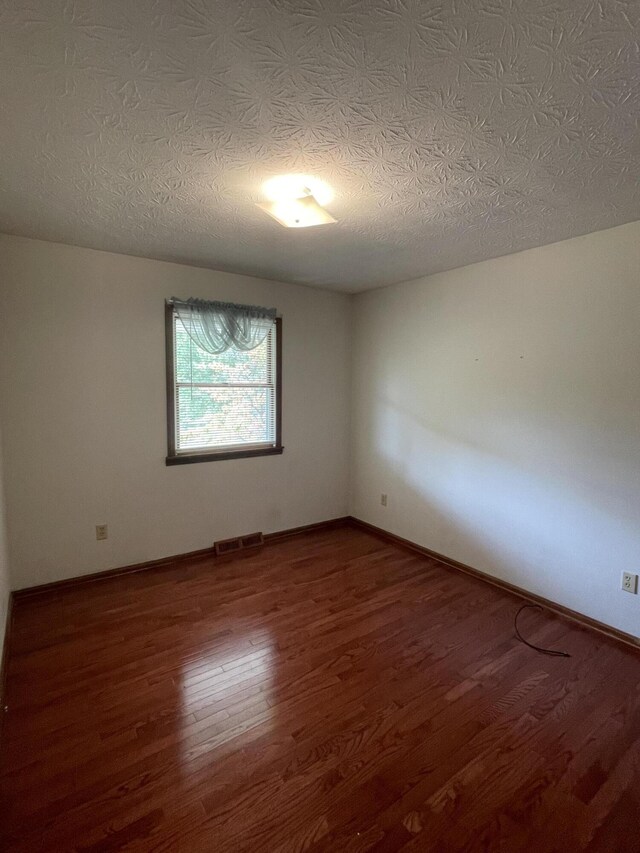 empty room with dark hardwood / wood-style flooring and a textured ceiling