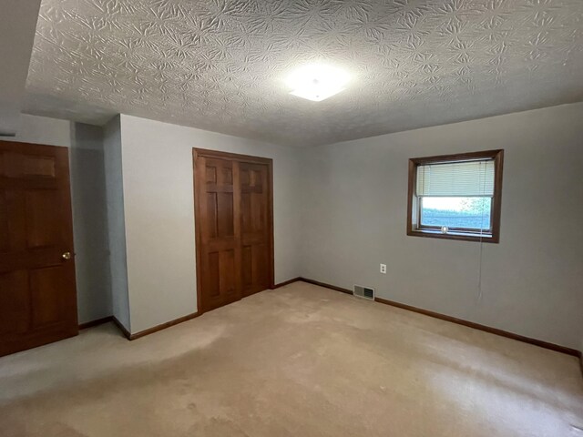 unfurnished bedroom with light colored carpet, a textured ceiling, and a closet