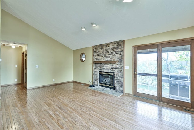 unfurnished living room with a stone fireplace, vaulted ceiling, and light wood-type flooring