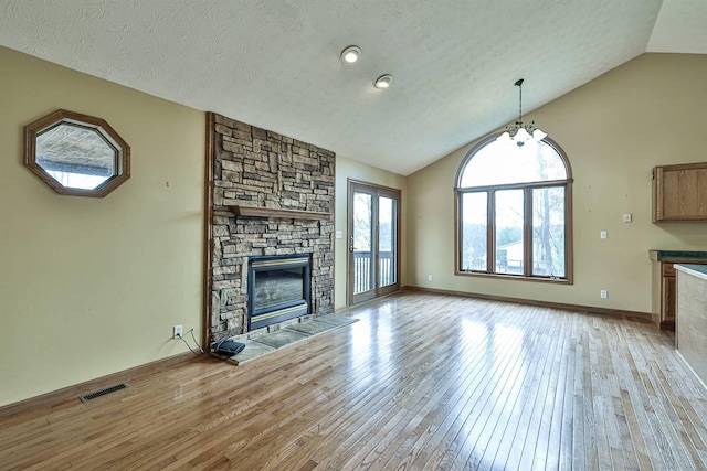 unfurnished living room with an inviting chandelier, vaulted ceiling, a stone fireplace, and light hardwood / wood-style flooring