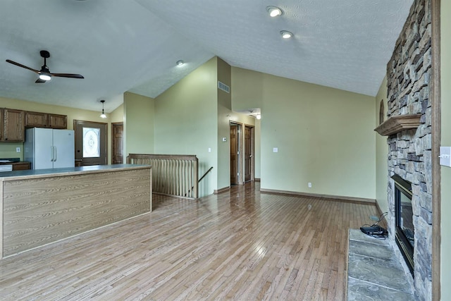 unfurnished living room featuring ceiling fan, a stone fireplace, light hardwood / wood-style flooring, lofted ceiling, and a textured ceiling