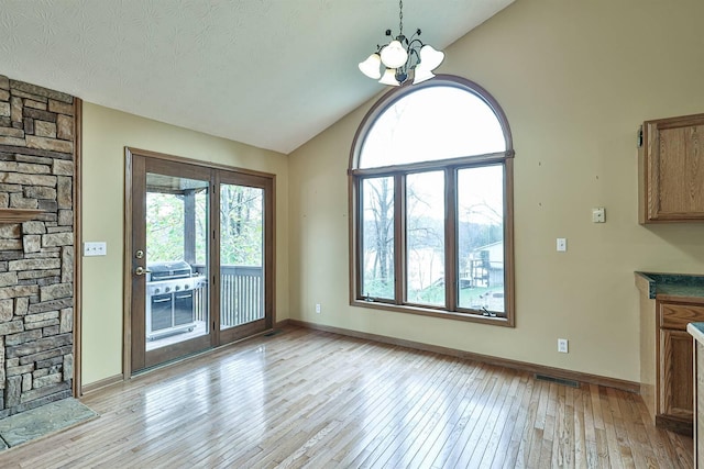 unfurnished dining area with light hardwood / wood-style floors, vaulted ceiling, and a notable chandelier