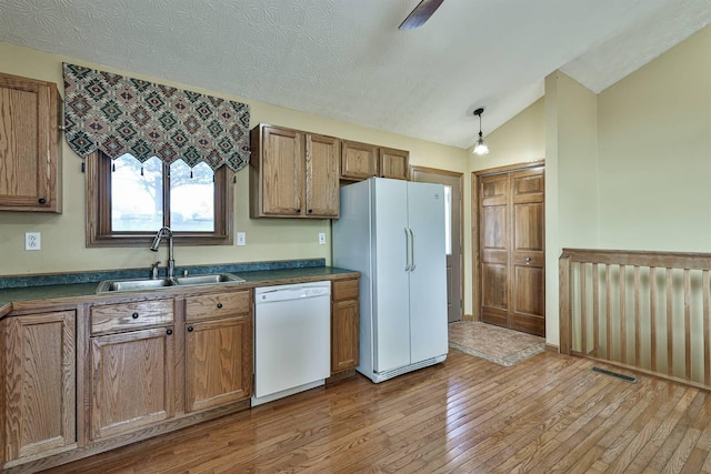 kitchen with sink, hanging light fixtures, vaulted ceiling, white appliances, and light wood-type flooring