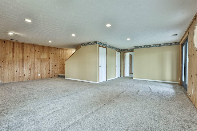 empty room with carpet flooring, a textured ceiling, and wooden walls