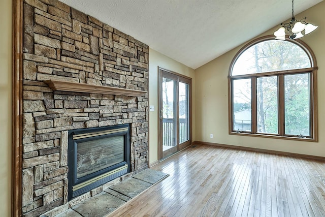 unfurnished living room featuring lofted ceiling, an inviting chandelier, a stone fireplace, a textured ceiling, and light hardwood / wood-style floors