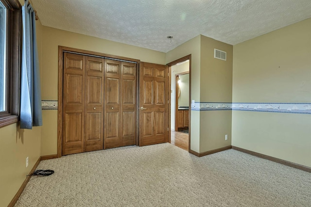 unfurnished bedroom featuring light carpet, a closet, and a textured ceiling