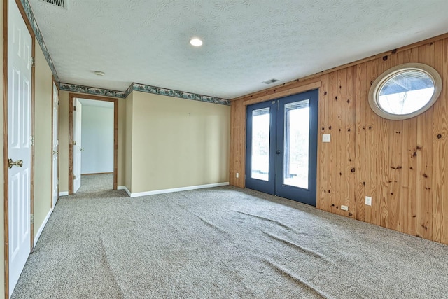 empty room with carpet flooring, french doors, a textured ceiling, and wooden walls