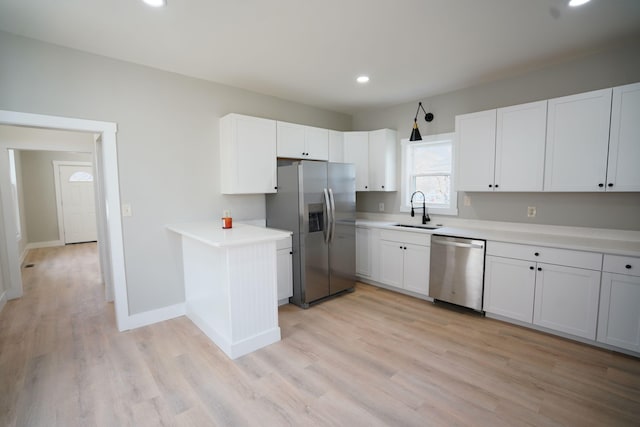 kitchen with sink, stainless steel appliances, kitchen peninsula, white cabinets, and light wood-type flooring