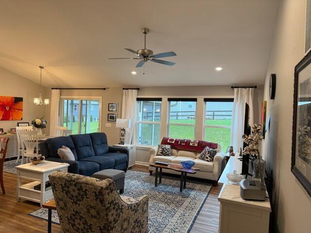 living room featuring vaulted ceiling, ceiling fan with notable chandelier, and hardwood / wood-style flooring