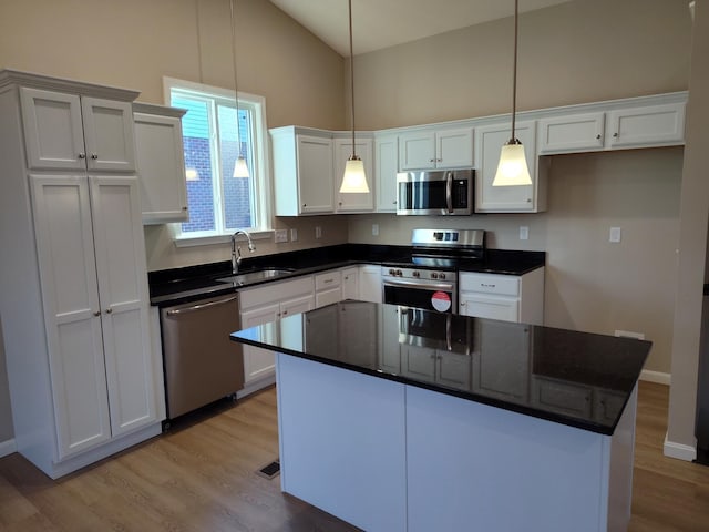 kitchen featuring a sink, white cabinetry, appliances with stainless steel finishes, a center island, and decorative light fixtures