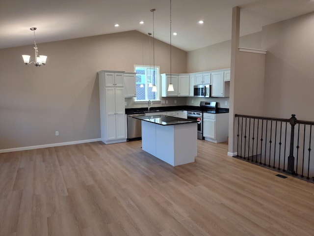 kitchen featuring white cabinets, dark countertops, a kitchen island, appliances with stainless steel finishes, and hanging light fixtures