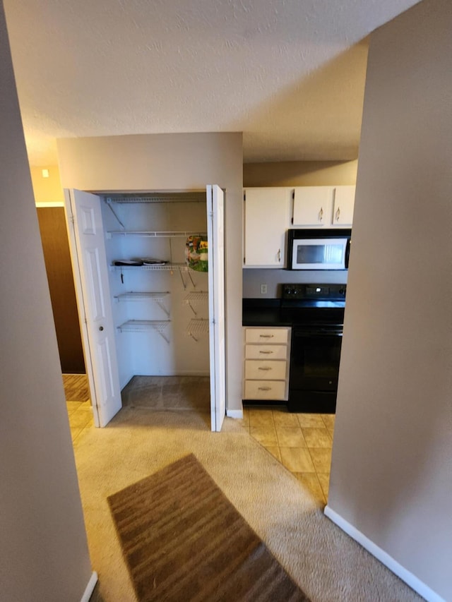 kitchen with electric range, white cabinets, light colored carpet, and a textured ceiling