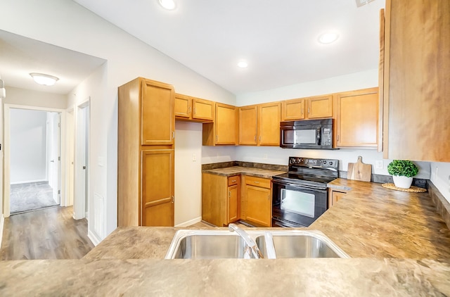 kitchen with sink, light hardwood / wood-style floors, vaulted ceiling, and black appliances