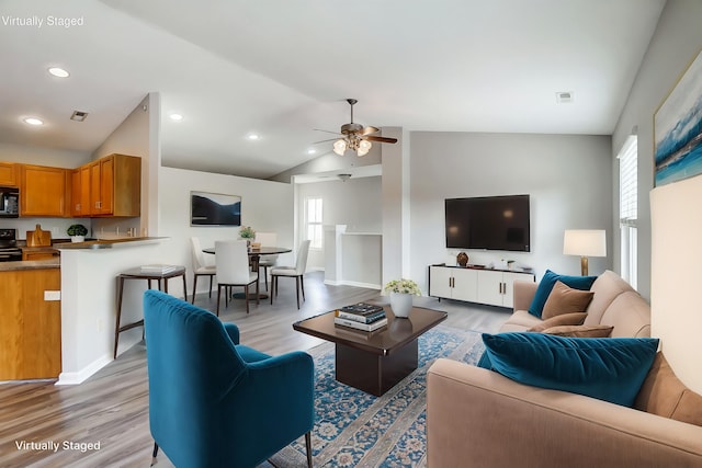 living room featuring light hardwood / wood-style floors, vaulted ceiling, and ceiling fan