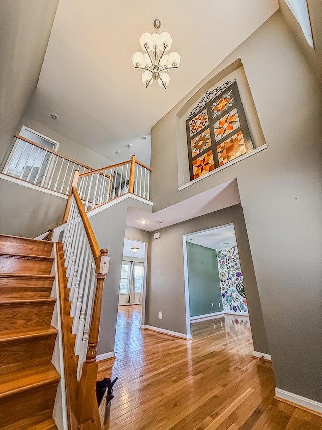 stairs with wood-type flooring, an inviting chandelier, and a high ceiling