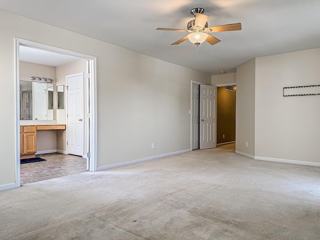 unfurnished bedroom featuring ceiling fan, built in desk, light carpet, and ensuite bath