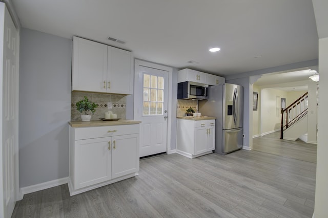 kitchen featuring decorative backsplash, white cabinetry, light wood-type flooring, and appliances with stainless steel finishes