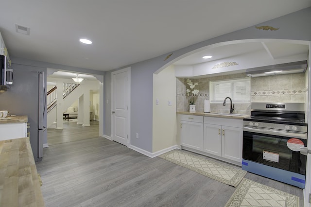 kitchen with gas range, white cabinetry, sink, backsplash, and exhaust hood