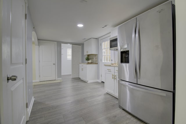 kitchen featuring stainless steel fridge, light wood-type flooring, white cabinetry, and backsplash