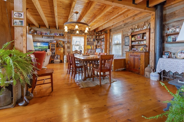 dining area featuring a notable chandelier, wood ceiling, a wood stove, beamed ceiling, and hardwood / wood-style flooring