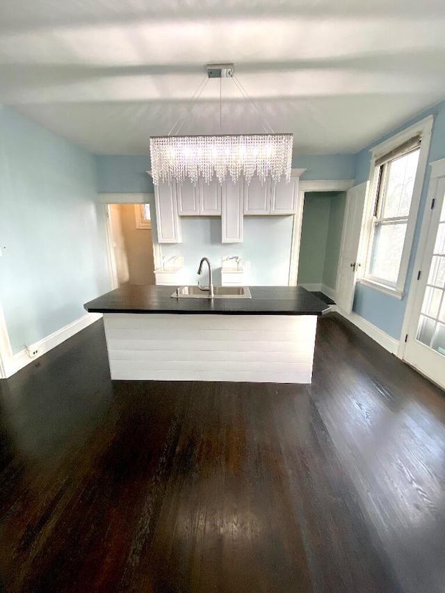 kitchen with white cabinetry, sink, dark wood-type flooring, an inviting chandelier, and pendant lighting