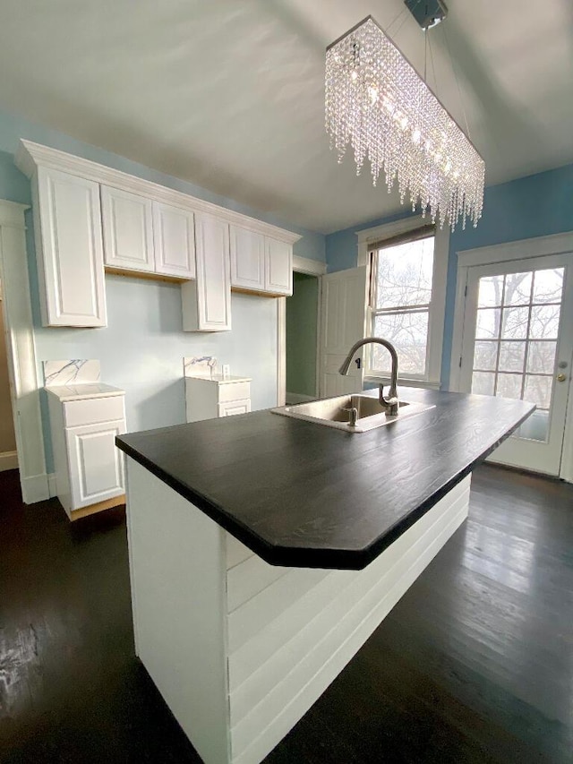 kitchen with white cabinets, dark wood-type flooring, a notable chandelier, and sink