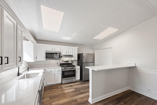 kitchen featuring kitchen peninsula, appliances with stainless steel finishes, dark hardwood / wood-style flooring, sink, and white cabinetry