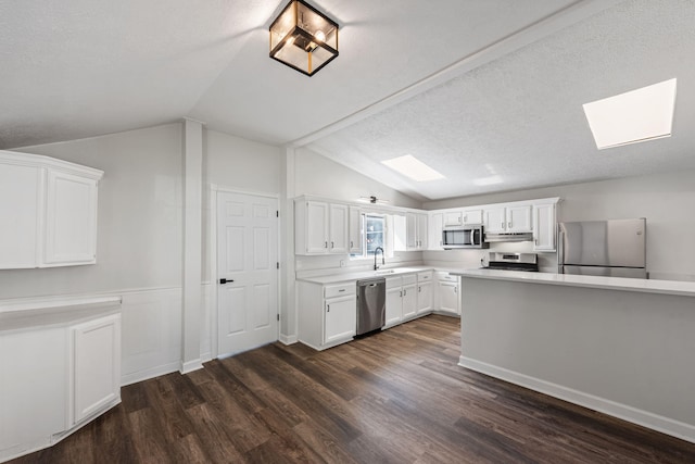 kitchen featuring a textured ceiling, white cabinetry, stainless steel appliances, and lofted ceiling with skylight