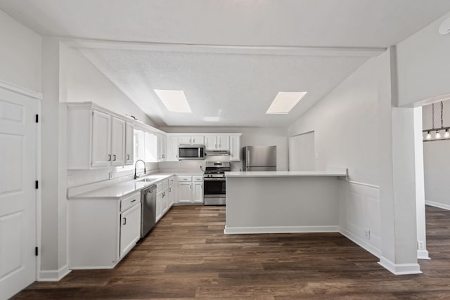 kitchen with dark wood-type flooring, white cabinets, sink, vaulted ceiling with skylight, and stainless steel appliances