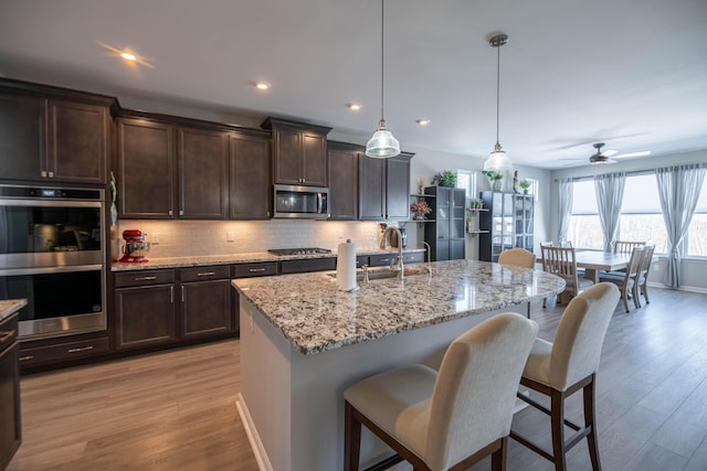 kitchen featuring a kitchen island with sink, a breakfast bar area, appliances with stainless steel finishes, hanging light fixtures, and ceiling fan