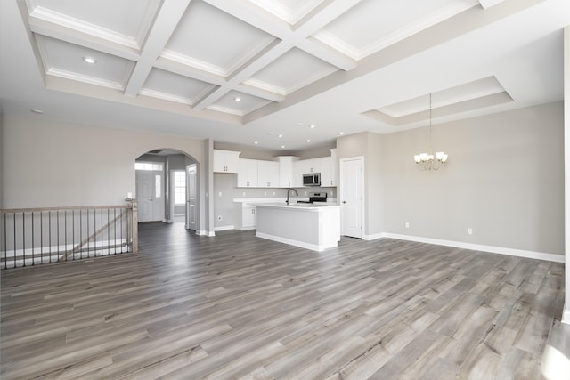 unfurnished living room with coffered ceiling, sink, beam ceiling, a chandelier, and light hardwood / wood-style floors