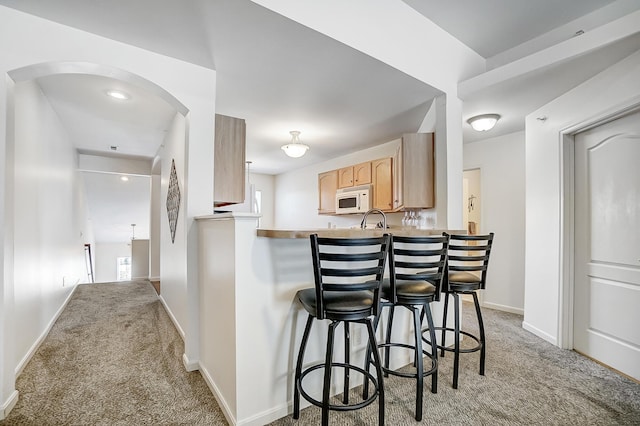 kitchen featuring sink, light brown cabinets, kitchen peninsula, light carpet, and a breakfast bar