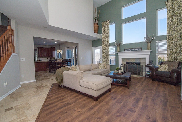 living room featuring a tiled fireplace, a towering ceiling, a wealth of natural light, and hardwood / wood-style floors