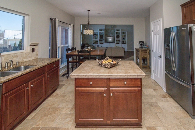 kitchen with a center island, decorative backsplash, sink, hanging light fixtures, and stainless steel fridge